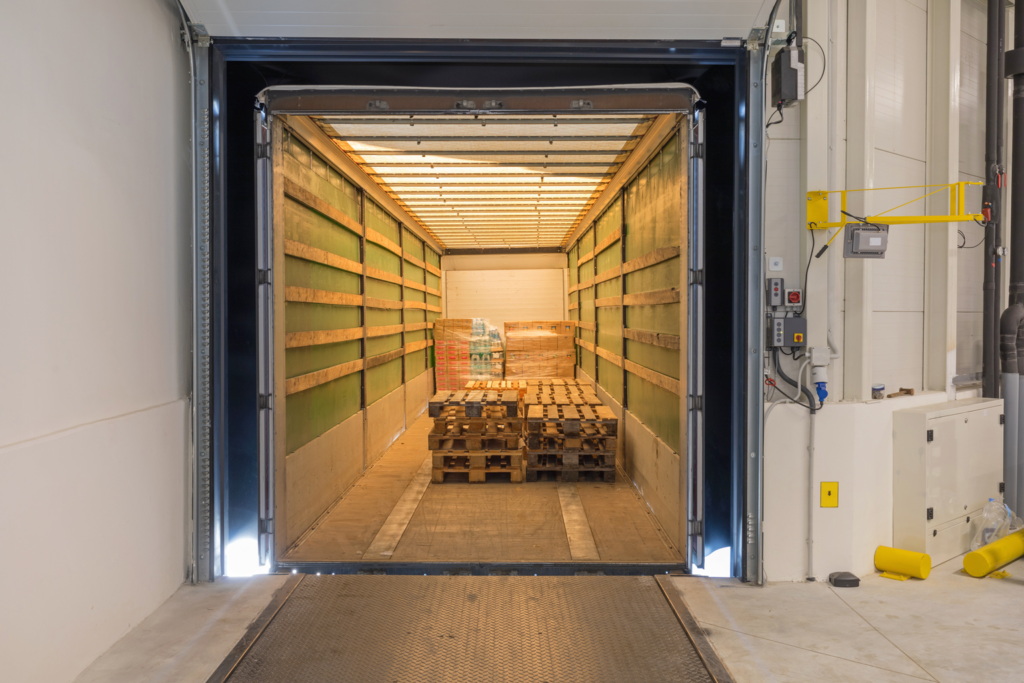 An almost empty trailer backed into a warehouse loading dock, the last pallets still inside, illustrating how warehouse security fails when freight leaves on a fraudulent pickup